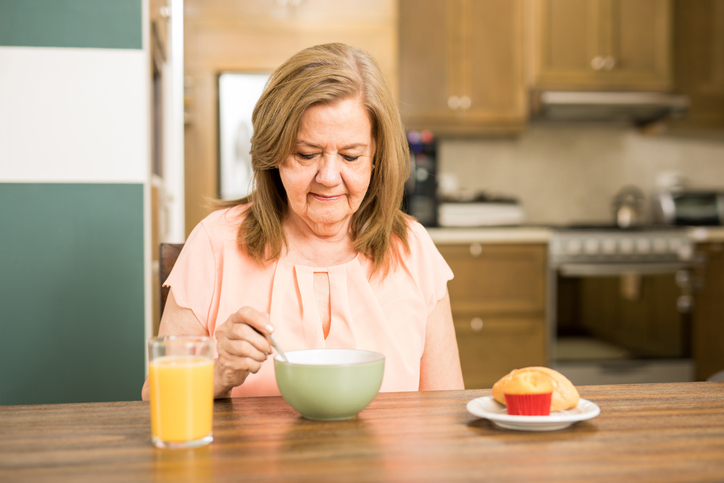 Pretty senior woman sitting in the kitchen and without appetite for breakfast