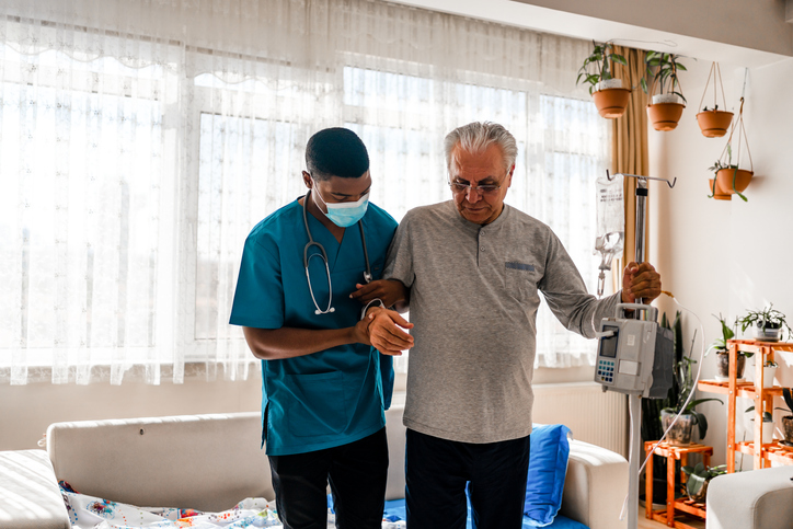 Health visitor helping a man get on his feet during a home visit