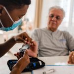 District male nurse at home visit taking their patient blood sugar