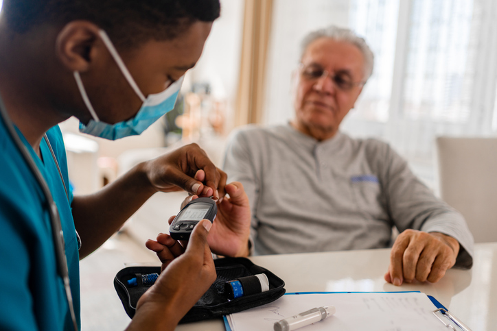 District male nurse at home visit taking their patient blood sugar