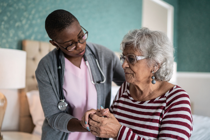 Home caregiver helping a senior woman standing in the bedroom.