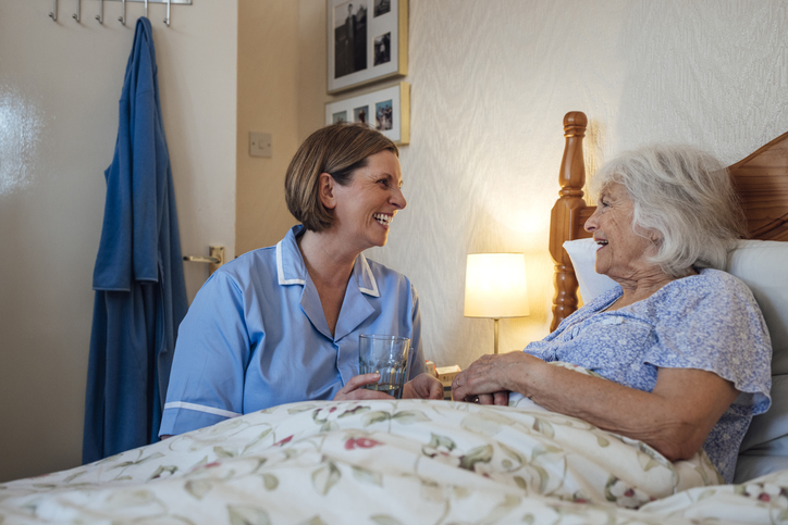 A female nurse assisting a female senior by her bed side