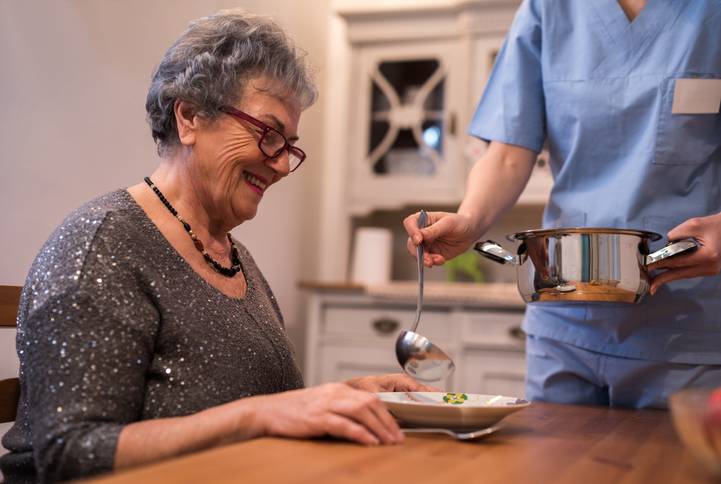 Unrecognisable nurse giving senior women to eat soup at home.